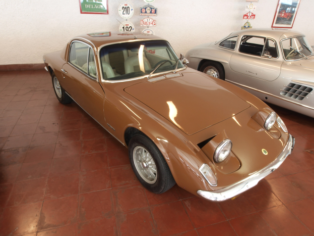 Zwei klassische Autos, ein Ferrari 250 GT und ein Ferrari Dino 246 GT, Seite an Seite in einem Raum mit Rahmenfotos und Tafeln an der Wand dahinter geparkt.