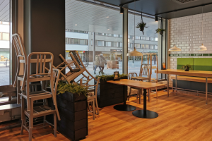 Ein Berliner Restaurant mit Holztischen und -stühlen vor einem großen Fenster, das Fußgänger, Gebäude und Straßenelemente zeigt.