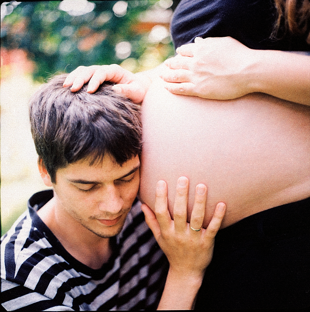 Ein Mann und eine Frau stehen nebeneinander, wobei der Mann zärtlich den Bauch der Frau berührt und sich auf ihr ungeborenes Kind konzentriert.
