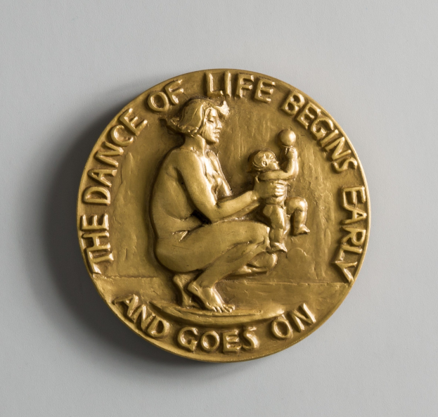 Eine Goldmedaille mit der Inschrift "Der Tanz des Lebens beginnt früh und geht weiter" und ein Bild einer Frau, die ein Baby hält.
