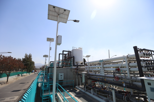 Großes industrielles Gebäude mit umfangreichen Rohrleitungen, Solarmodulen, Geländern und Infrastruktur, umgeben von Hügeln unter einem klaren blauen Himmel, Teil der neuen Wasseraufbereitungsanlage von Kalifornien.