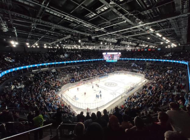 Eishockeyspiel in einer großen Arena mit Zuschauern auf den Rängen und Mitarbeitern am Boden, mit Geländern, Deckenbeleuchtung und einem Bildschirm in der O2 Arena in London.