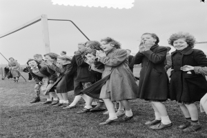 Schwarzes Bild von Kindern, die auf einem Feld mit einem Tor im Hintergrund unter einem klaren Himmel klatschen.
