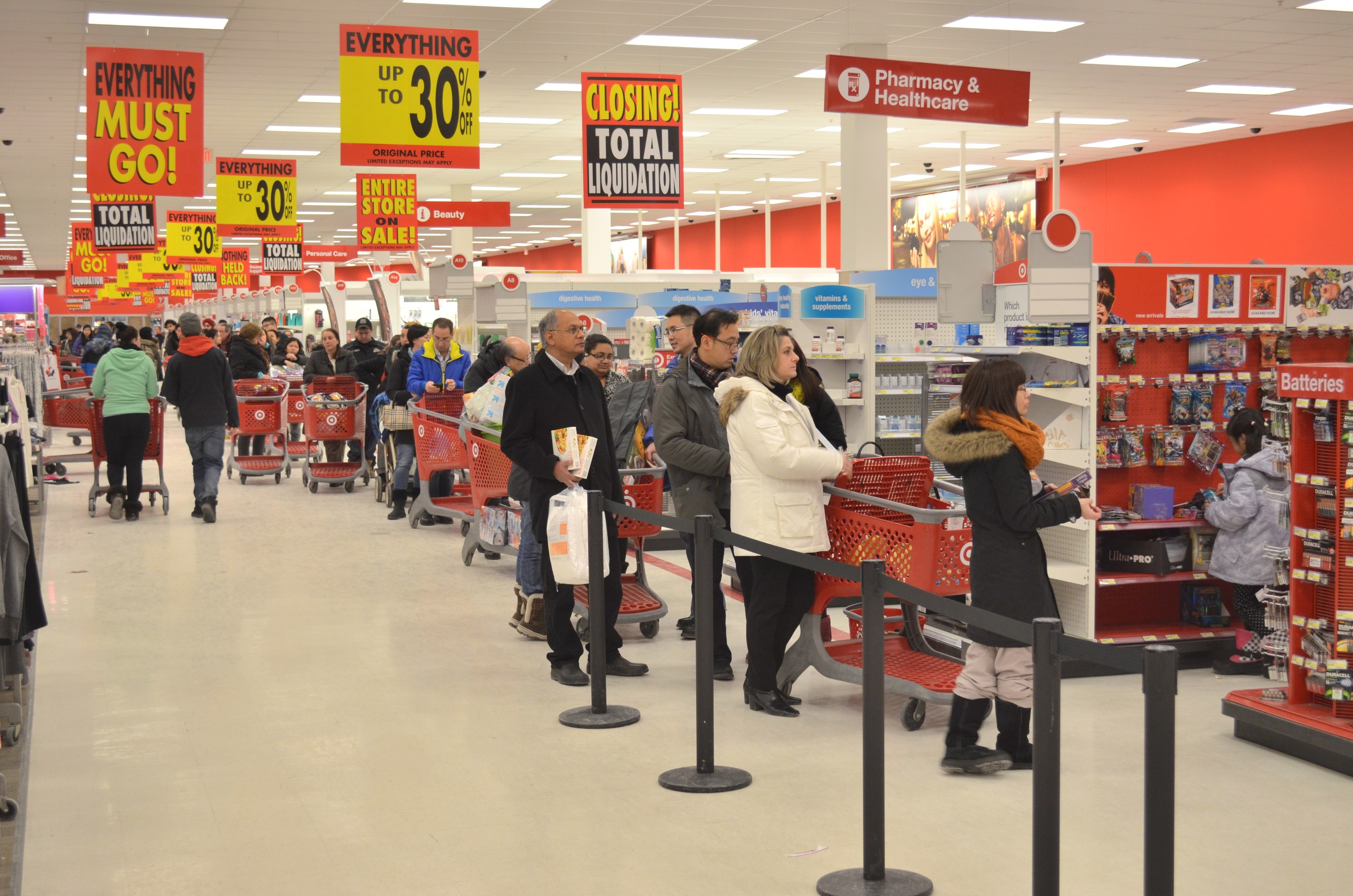 Ein überfüllter Walmart-Laden mit Einkaufstüten tragenden Kunden und Einkaufswagen, umgeben von Warenpräsentationen, Schildern und Deckenleuchten, wahrscheinlich während eines Black Friday-Verkaufs.