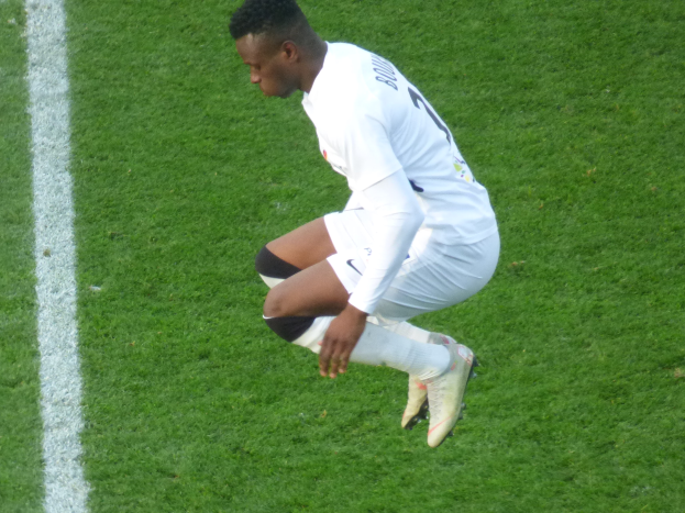 Ein Mann in weißer Uniform kniet auf einem Fußballfeld und trägt Fußballschuhe.