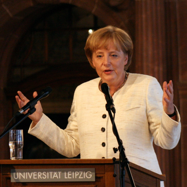 Bundeskanzlerin Angela Merkel hält eine Rede an der Universität Leipzig und steht hinter einem Rednerpult mit Mikrofon und einem Glas Wasser.