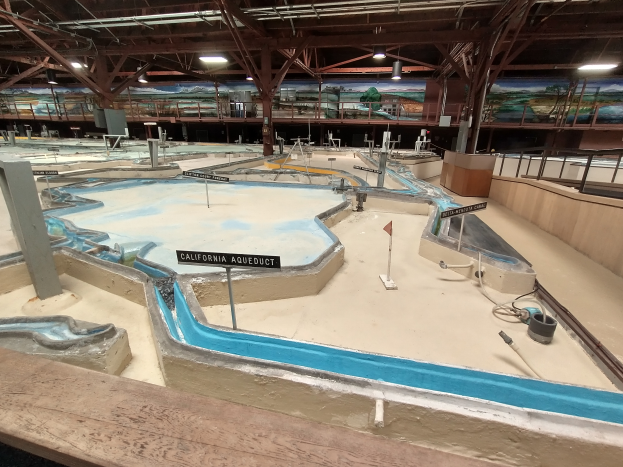 Ein großer Indoor-Wasserpark mit zahlreichen Wasserrutschen, Pfählen, Schildern, Deckenleuchten und Wandgemälden, der einem Minigolfplatz ähnelt.