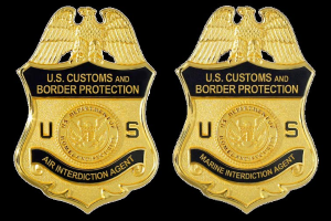 Zwei goldfarbene Abzeichen mit 'U.S. Customs and Border Protection'-Text auf weißem Hintergrund.