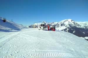 Ein Hubschrauber auf einem schneebedeckten Berg geparkt mit ein paar Menschen in der Nähe, unter einem klaren Himmel.