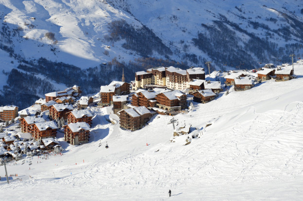 Eine malerische Ansicht eines Skigebiets in den französischen Alpen mit schneebedeckten Bergen, Gebäuden, Bäumen und Skifahrern auf den Pisten.