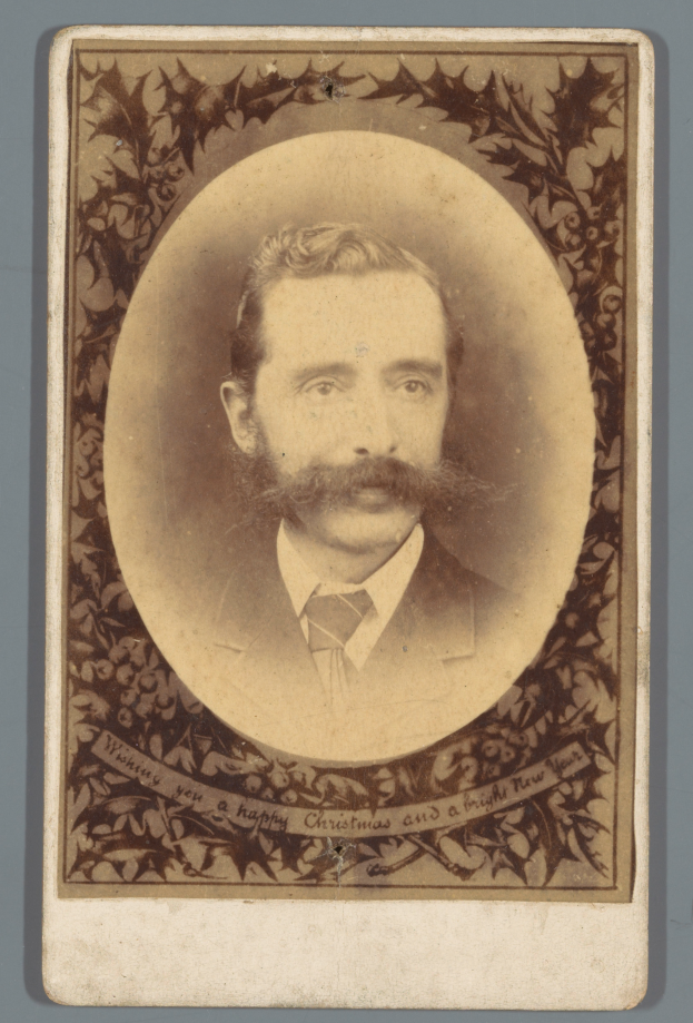 Ein altes Foto eines Mannes mit Schnurrbart und Bart, der einen Anzug und eine Krawatte trägt und ernst in die Kamera schaut.