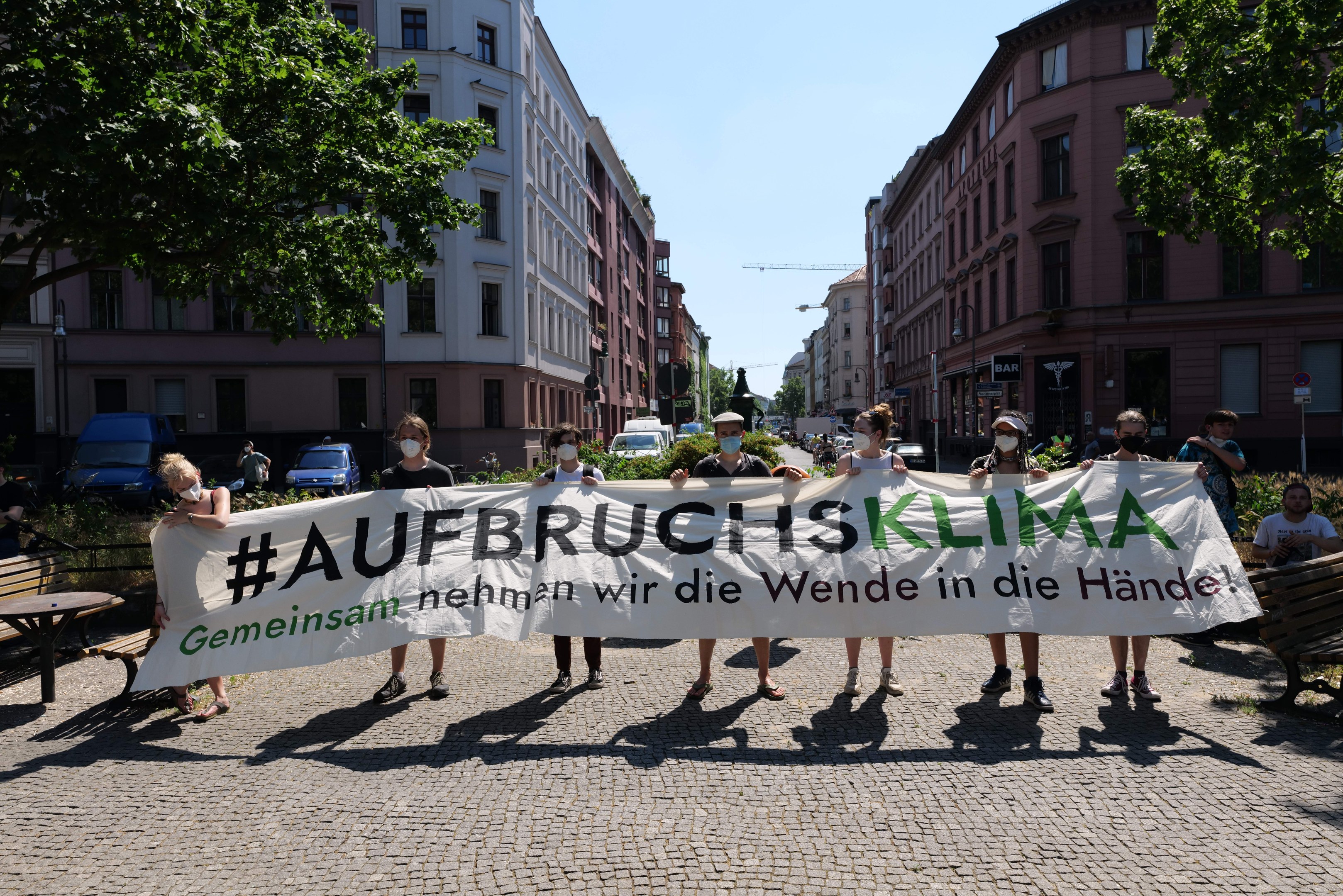 Menschen mit Masken halten ein Banner mit der Aufschrift 'Aufbruchsklima' während einer Klimaprotest in Berlin, umgeben von städtischen Elementen und anderen Teilnehmern.